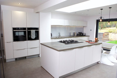 Photo of a large contemporary u-shaped open plan kitchen in Sussex with a built-in sink, beaded cabinets, white cabinets, wood worktops, integrated appliances, laminate floors, an island and grey floors.