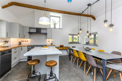 Medium sized rural l-shaped open plan kitchen in Cornwall with a built-in sink, shaker cabinets, grey cabinets, concrete worktops, white splashback, black appliances, slate flooring, an island, black floors, white worktops and exposed beams.