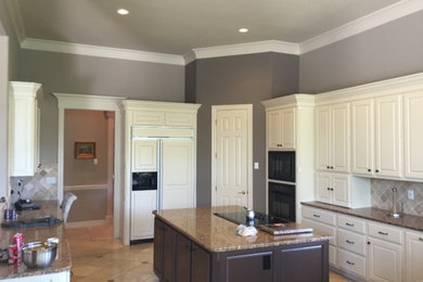 Example of a large transitional u-shaped enclosed kitchen design in Austin with raised-panel cabinets, white cabinets, granite countertops, beige backsplash, porcelain backsplash, paneled appliances, an island and multicolored countertops