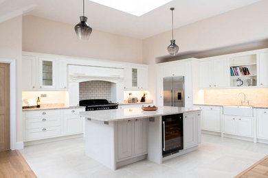 Photo of a large grey and white l-shaped kitchen/diner in Sussex with a double-bowl sink, shaker cabinets, white cabinets, quartz worktops, white splashback, metro tiled splashback, stainless steel appliances, ceramic flooring, an island, grey floors, multicoloured worktops and feature lighting.