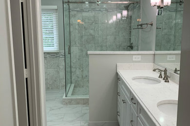 Photo of a large contemporary master bathroom in DC Metro with flat-panel cabinets, white cabinets, a drop-in tub, a corner shower, a two-piece toilet, multi-coloured tile, marble, grey walls, porcelain floors, an undermount sink, engineered quartz benchtops, white floor, a sliding shower screen and white benchtops.