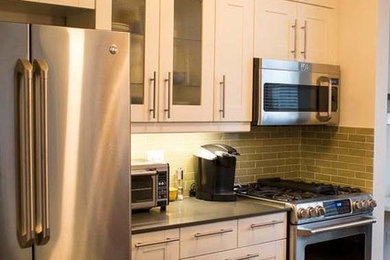 Example of a mid-sized minimalist slate floor kitchen design in New York with shaker cabinets, white cabinets, granite countertops, green backsplash, stainless steel appliances and a peninsula