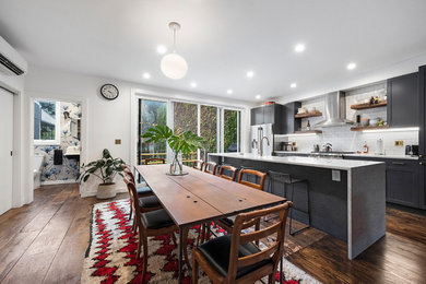 Photo of a contemporary galley eat-in kitchen in New York with shaker cabinets, grey cabinets, white splashback, subway tile splashback, stainless steel appliances, dark hardwood floors, with island, brown floor and grey benchtop.