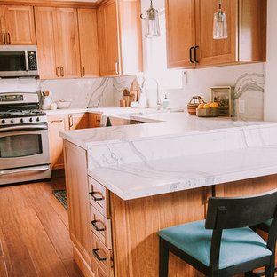 Cette photo montre une arrière-cuisine montagne en L de taille moyenne avec un évier de ferme, un placard à porte shaker, des portes de placard en bois brun, un plan de travail en quartz modifié, une crédence blanche, une crédence en dalle de pierre, un électroménager en acier inoxydable, un sol en bambou, une péninsule, un sol marron et un plan de travail blanc.