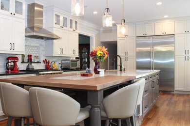 Example of a large transitional dark wood floor and brown floor eat-in kitchen design in New York with a farmhouse sink, recessed-panel cabinets, gray cabinets, wood countertops, white backsplash, marble backsplash, stainless steel appliances and an island