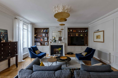 Cette image montre un grand salon traditionnel avec une bibliothèque ou un coin lecture, un mur blanc, parquet clair, une cheminée standard, un manteau de cheminée en plâtre et un téléviseur encastré.