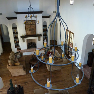 Foto de salón para visitas cerrado, mediterráneo, grande, con paredes blancas, suelo de madera en tonos medios, chimenea tradicional, marco de chimenea de hormigón, pared multimedia y suelo marrón