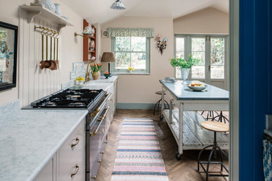 This is an example of a mid-sized traditional single-wall eat-in kitchen in London with a farmhouse sink, shaker cabinets, beige cabinets, quartzite benchtops, beige splashback, black appliances, with island, brown floor and grey benchtop.