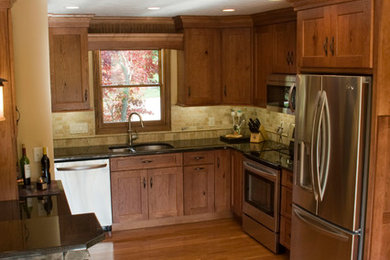 Inspiration for a mid-sized timeless l-shaped light wood floor eat-in kitchen remodel in Other with an undermount sink, shaker cabinets, medium tone wood cabinets, granite countertops, beige backsplash, stone tile backsplash, stainless steel appliances and no island