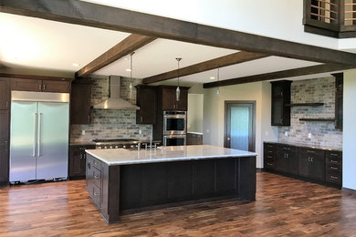 Photo of a large transitional single-wall open plan kitchen in Milwaukee with a farmhouse sink, shaker cabinets, dark wood cabinets, grey splashback, stainless steel appliances, dark hardwood floors, with island, brown floor, onyx benchtops and brick splashback.