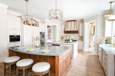 Inspiration for a large french country u-shaped light wood floor and brown floor eat-in kitchen remodel in Houston with a farmhouse sink, recessed-panel cabinets, white cabinets, granite countertops, beige backsplash, mosaic tile backsplash, paneled appliances, two islands and white countertops