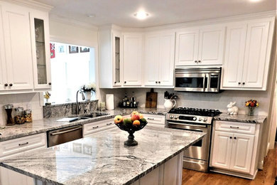 This is an example of a mid-sized transitional u-shaped open plan kitchen in Atlanta with an undermount sink, raised-panel cabinets, white cabinets, marble benchtops, white splashback, porcelain splashback, stainless steel appliances, medium hardwood floors, with island, brown floor and grey benchtop.