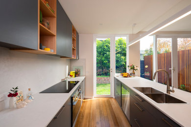 Mid-sized contemporary galley open plan kitchen in Melbourne with a drop-in sink, flat-panel cabinets, grey cabinets, granite benchtops, white splashback, granite splashback, stainless steel appliances, medium hardwood floors, with island, brown floor and white benchtop.