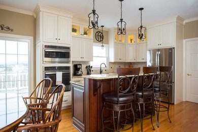 Mid-sized elegant l-shaped medium tone wood floor eat-in kitchen photo in New Orleans with raised-panel cabinets, white cabinets, granite countertops, beige backsplash, stone tile backsplash, stainless steel appliances, an island and a double-bowl sink