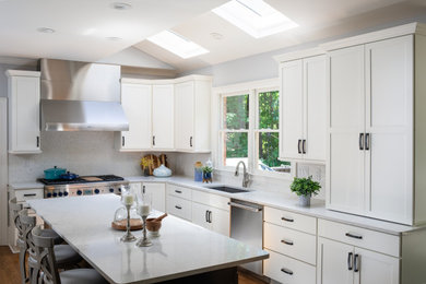 Example of a mid-sized transitional l-shaped medium tone wood floor and brown floor eat-in kitchen design in Atlanta with a single-bowl sink, shaker cabinets, white cabinets, quartz countertops, metallic backsplash, mosaic tile backsplash, stainless steel appliances, an island and white countertops