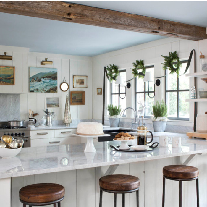 Picture-Perfect Christmas Kitchen. bright kitchen gets pops of green from wreaths above the windows, a velvet ribbon swag, and potted rosemary. Picture lights illuminate the art collection.