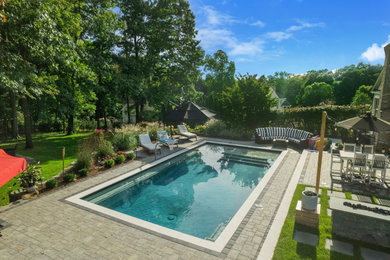Ejemplo de piscina clásica grande rectangular en patio trasero con paisajismo de piscina y adoquines de piedra natural