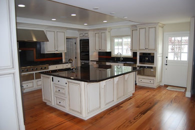 Inspiration for a large transitional u-shaped kitchen in Orange County with raised-panel cabinets, distressed cabinets, solid surface benchtops, black splashback, medium hardwood floors, with island and brown floor.