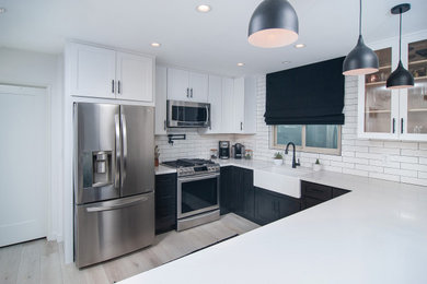 Example of a mid-sized country u-shaped light wood floor and brown floor enclosed kitchen design in San Diego with a farmhouse sink, shaker cabinets, black cabinets, quartz countertops, white backsplash, subway tile backsplash, stainless steel appliances, a peninsula and white countertops