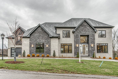 Large contemporary gray two-story brick exterior home idea in Other with a shingle roof