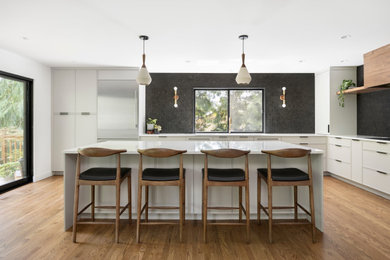 Large 1960s l-shaped medium tone wood floor and brown floor eat-in kitchen photo in Portland with an undermount sink, recessed-panel cabinets, gray cabinets, quartz countertops, black backsplash, mosaic tile backsplash, stainless steel appliances, an island and white countertops