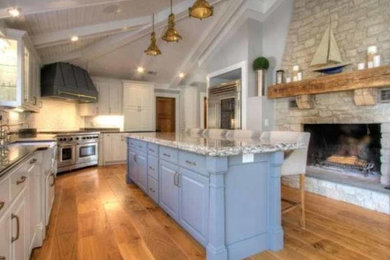 Large elegant single-wall light wood floor eat-in kitchen photo with a farmhouse sink, raised-panel cabinets, white cabinets, granite countertops, white backsplash, subway tile backsplash, stainless steel appliances and an island