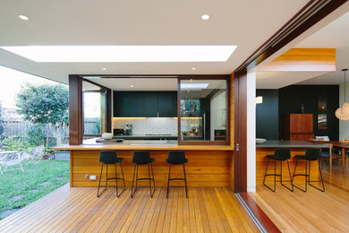 Design ideas for a mid-sized contemporary u-shaped open plan kitchen in Sydney with an integrated sink, flat-panel cabinets, black cabinets, concrete benchtops, white splashback, medium hardwood floors and no island.