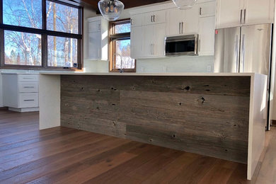 Large minimalist l-shaped medium tone wood floor and brown floor eat-in kitchen photo in Other with a drop-in sink, shaker cabinets, white cabinets, solid surface countertops, white backsplash, ceramic backsplash, stainless steel appliances, an island and white countertops