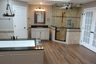 Photo of a large transitional master bathroom in DC Metro with grey walls, brown floor, raised-panel cabinets, beige cabinets, an undermount tub, a corner shower, beige tile, ceramic tile, porcelain floors, an undermount sink, granite benchtops, a hinged shower door and black benchtops.