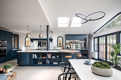 Inspiration for a large modern l-shaped open plan kitchen in London with an integrated sink, shaker cabinets, blue cabinets, composite countertops, white splashback, integrated appliances, ceramic flooring, an island, beige floors, white worktops and feature lighting.