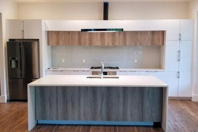 Example of a mid-sized minimalist single-wall brown floor and medium tone wood floor eat-in kitchen design in Miami with flat-panel cabinets, white cabinets, an island, white countertops, an undermount sink, stainless steel appliances, quartz countertops, white backsplash and glass sheet backsplash