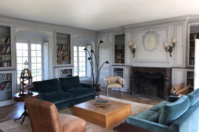 Cette photo montre un salon chic avec une bibliothèque ou un coin lecture, un mur gris, un sol en bois brun, une cheminée standard et boiseries.