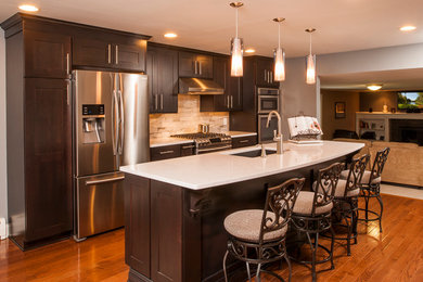 Mid-sized elegant single-wall medium tone wood floor eat-in kitchen photo in New York with an undermount sink, recessed-panel cabinets, dark wood cabinets, quartz countertops, beige backsplash, ceramic backsplash, stainless steel appliances and an island
