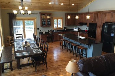 Large mountain style l-shaped medium tone wood floor and brown floor open concept kitchen photo in New York with a farmhouse sink, shaker cabinets, medium tone wood cabinets, granite countertops, black appliances and an island