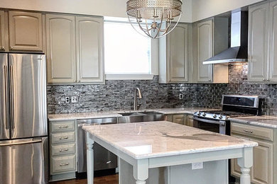 This is an example of a mid-sized contemporary l-shaped eat-in kitchen in New Orleans with a double-bowl sink, raised-panel cabinets, grey cabinets, marble benchtops, metallic splashback, subway tile splashback, stainless steel appliances, dark hardwood floors, with island and brown floor.