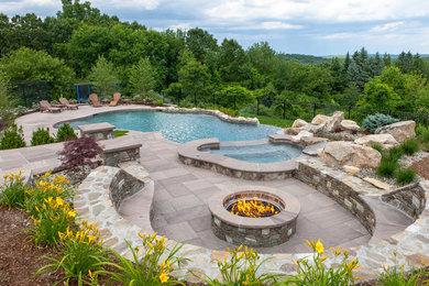 This is an example of a mid-sized traditional backyard custom-shaped natural pool in Boston with a water feature and natural stone pavers.