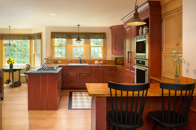 Design ideas for a large country l-shaped separate kitchen in Portland Maine with a drop-in sink, raised-panel cabinets, brown cabinets, wood benchtops, stainless steel appliances, light hardwood floors, a peninsula, brown floor and brown benchtop.