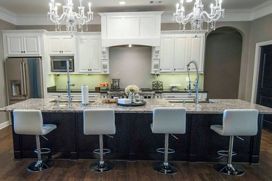 Photo of a large traditional single-wall eat-in kitchen in Other with white cabinets, granite benchtops, a farmhouse sink, stainless steel appliances, dark hardwood floors, with island, raised-panel cabinets, green splashback and brown floor.