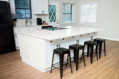 Example of a mid-sized minimalist light wood floor, brown floor and wood ceiling eat-in kitchen design in Dallas with a single-bowl sink, recessed-panel cabinets, white cabinets, quartzite countertops, white backsplash, ceramic backsplash, stainless steel appliances, an island and white countertops