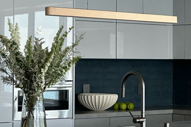 Eat-in kitchen - mid-sized modern l-shaped light wood floor eat-in kitchen idea in Seattle with a single-bowl sink, flat-panel cabinets, stainless steel cabinets, quartz countertops, blue backsplash, glass tile backsplash, stainless steel appliances, an island and gray countertops