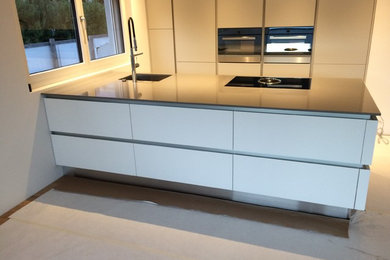 Immagine di una cucina minimalista di medie dimensioni con lavello sottopiano, ante lisce, ante bianche, top in quarzo composito, paraspruzzi nero e elettrodomestici neri