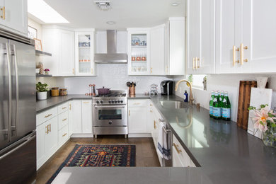 Mid-sized transitional u-shaped medium tone wood floor and brown floor enclosed kitchen photo in Los Angeles with an undermount sink, shaker cabinets, white cabinets, concrete countertops, white backsplash, stone slab backsplash, stainless steel appliances and a peninsula