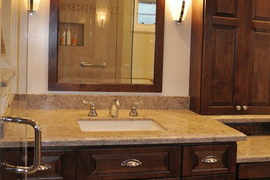 Elegant master beige tile ceramic tile corner shower photo in Los Angeles with raised-panel cabinets, medium tone wood cabinets, an undermount tub, a one-piece toilet, beige walls, a drop-in sink and quartz countertops