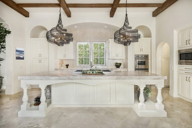 Example of a large minimalist l-shaped travertine floor, beige floor and exposed beam open concept kitchen design in Orange County with a farmhouse sink, raised-panel cabinets, white cabinets, quartzite countertops, beige backsplash, glass tile backsplash, an island and gray countertops