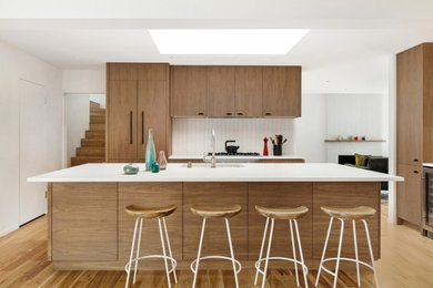 Inspiration for a midcentury kitchen in San Francisco with an integrated sink, flat-panel cabinets, medium wood cabinets, granite benchtops, white splashback, ceramic splashback, panelled appliances, light hardwood floors, with island, brown floor and white benchtop.