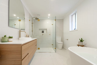 Design ideas for a large beach style kids bathroom in Sydney with flat-panel cabinets, medium wood cabinets, a freestanding tub, a corner shower, a two-piece toilet, white walls, a vessel sink, grey floor, a hinged shower door, a niche, a single vanity, a floating vanity and panelled walls.