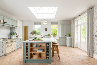 Large traditional kitchen/diner in Other with a belfast sink, shaker cabinets, green cabinets, marble worktops, white splashback, black appliances, brick flooring, an island, red floors, white worktops and a feature wall.