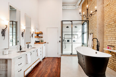 Industrial master bathroom in Other with flat-panel cabinets, distressed cabinets, a freestanding tub, a double shower, gray tile, ceramic tile, white walls, laminate floors, an undermount sink, quartzite benchtops, brown floor, a hinged shower door and white benchtops.
