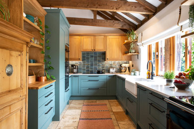 Photo of a medium sized rural u-shaped open plan kitchen in Kent with a belfast sink, shaker cabinets, green cabinets, quartz worktops, green splashback, ceramic splashback, black appliances, terracotta flooring, no island, orange floors, white worktops and exposed beams.