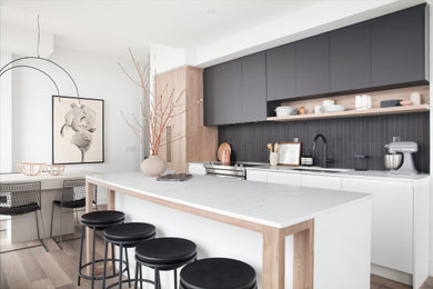 Example of a small trendy galley laminate floor and brown floor eat-in kitchen design in Toronto with an undermount sink, flat-panel cabinets, white cabinets, laminate countertops, black backsplash, glass tile backsplash, stainless steel appliances, an island and white countertops